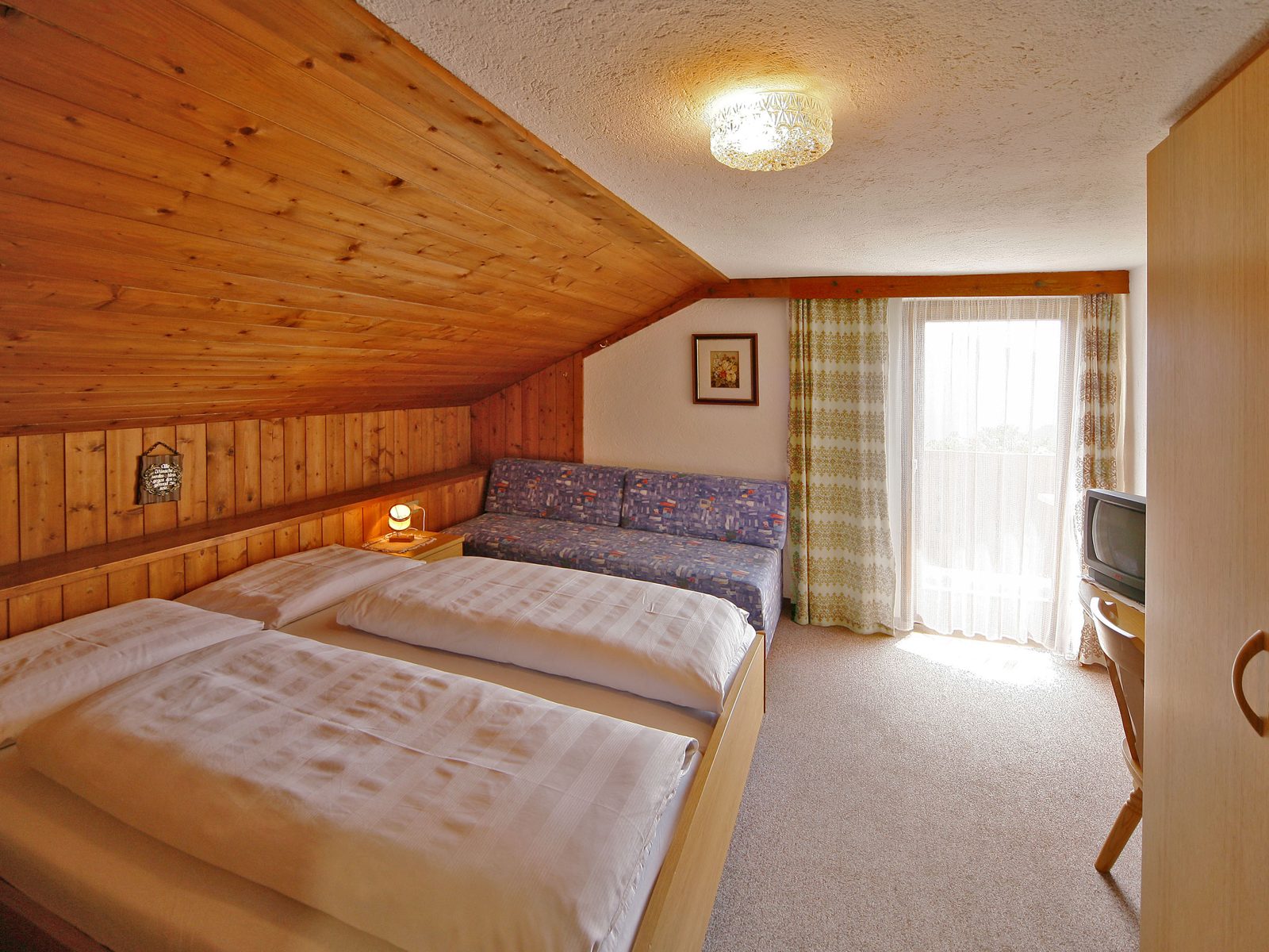 Zimmer mit Holzdachschräge, Bett, Schlafcouch und Balkontür